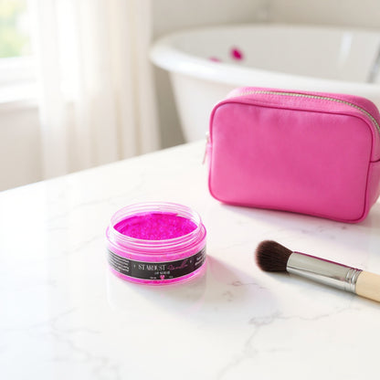 Pink makeup product, brush, and pink pouch on a marble surface
